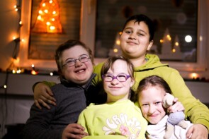 Vier Kinder sitzen eng zusammen und halten die Arme umeinander. Sie lachen in die Kamera.